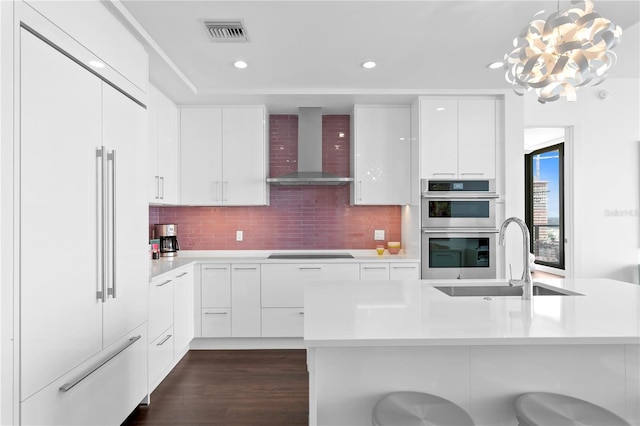 kitchen featuring pendant lighting, wall chimney exhaust hood, white cabinetry, tasteful backsplash, and paneled fridge