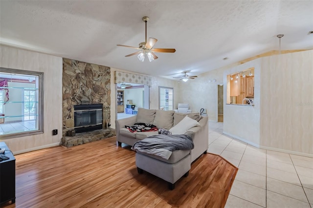 living room featuring a textured ceiling, ceiling fan, light tile patterned flooring, and a stone fireplace