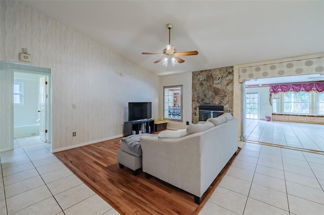 tiled living room featuring ceiling fan and a stone fireplace