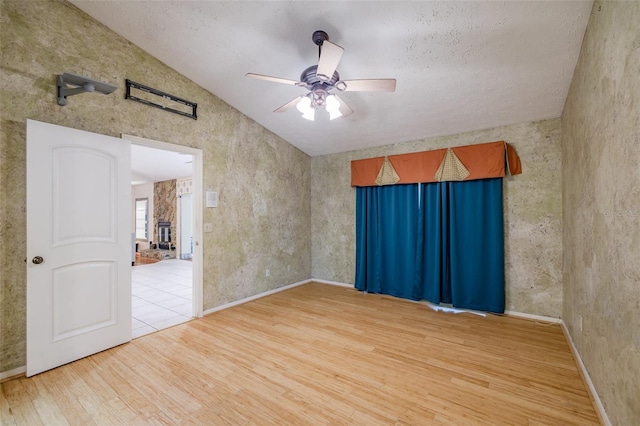 unfurnished room with ceiling fan, lofted ceiling, hardwood / wood-style floors, and a stone fireplace