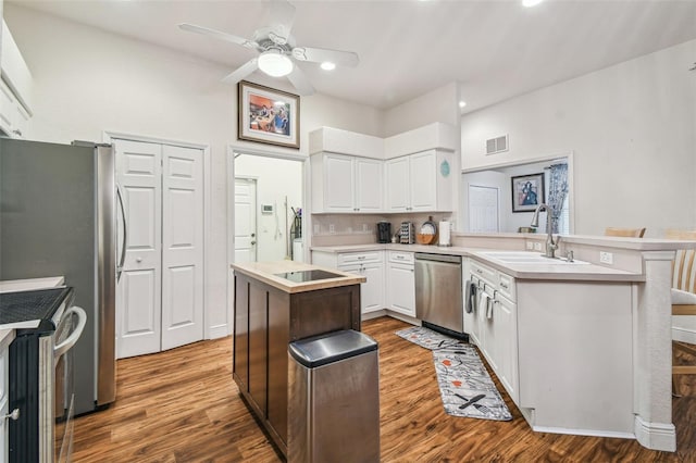 kitchen with wood-type flooring, sink, white cabinets, kitchen peninsula, and stainless steel appliances