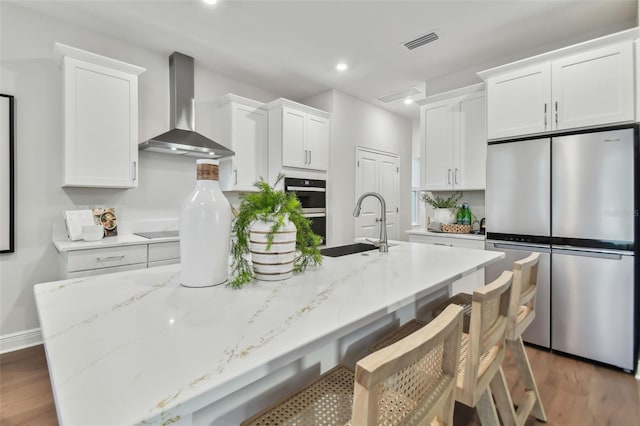 kitchen featuring white cabinetry, stainless steel appliances, a kitchen island with sink, wall chimney exhaust hood, and sink