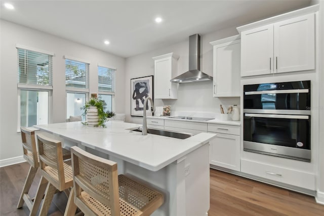 kitchen featuring sink, white cabinets, double oven, wall chimney exhaust hood, and black electric cooktop