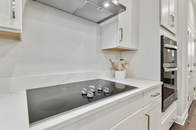 kitchen featuring white cabinetry, wall chimney range hood, and black electric cooktop