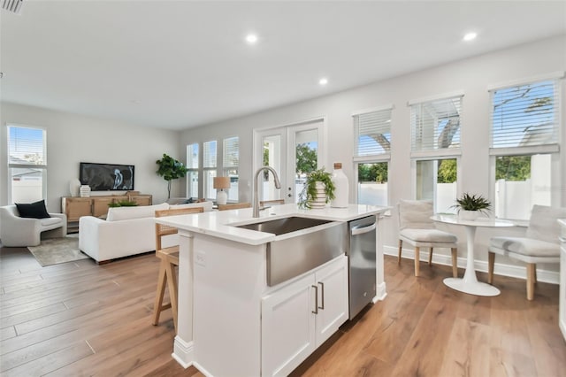 kitchen with dishwasher, sink, light wood-type flooring, a kitchen island with sink, and white cabinets