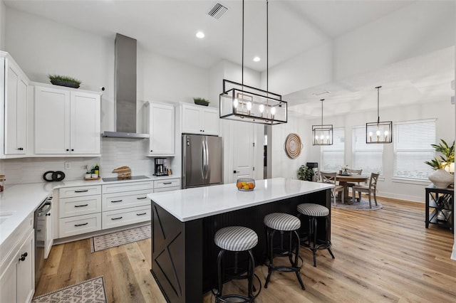 kitchen with a breakfast bar area, white cabinetry, black appliances, a kitchen island, and wall chimney exhaust hood