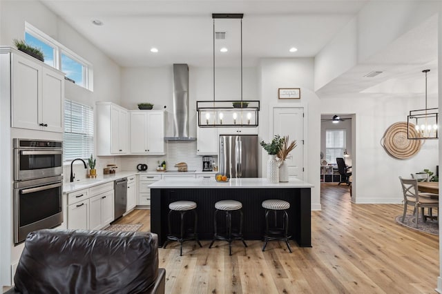 kitchen with pendant lighting, wall chimney range hood, a breakfast bar area, stainless steel appliances, and a kitchen island