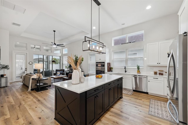 kitchen featuring a kitchen island, pendant lighting, white cabinets, a tray ceiling, and stainless steel appliances