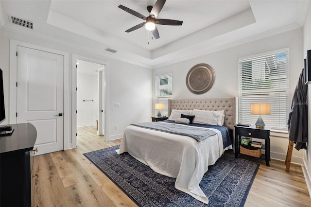 bedroom featuring ceiling fan, a tray ceiling, and light wood-type flooring