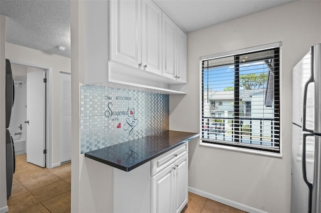 kitchen with dark countertops, decorative backsplash, freestanding refrigerator, white cabinets, and baseboards