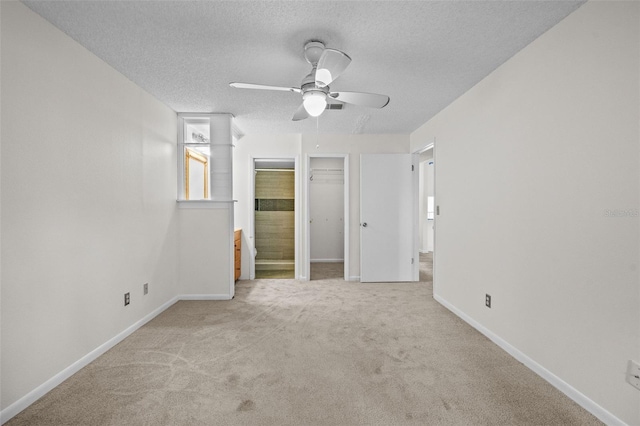 unfurnished bedroom with a spacious closet, a ceiling fan, light carpet, a textured ceiling, and baseboards