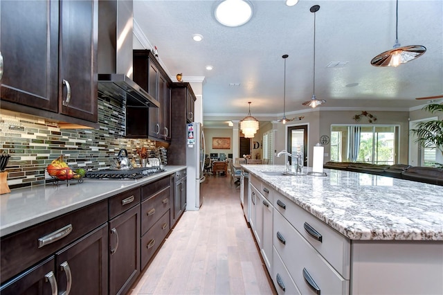 kitchen featuring wall chimney range hood, pendant lighting, a kitchen island with sink, stainless steel appliances, and white cabinets