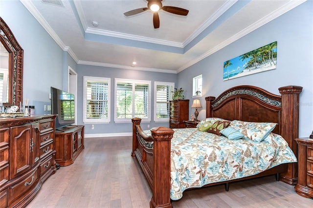 bedroom featuring ceiling fan, a raised ceiling, ornamental molding, and light wood-type flooring