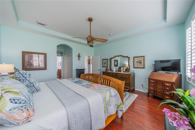 bedroom with a raised ceiling, dark wood-type flooring, and ceiling fan