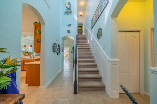 staircase with a towering ceiling, tile patterned floors, and sink