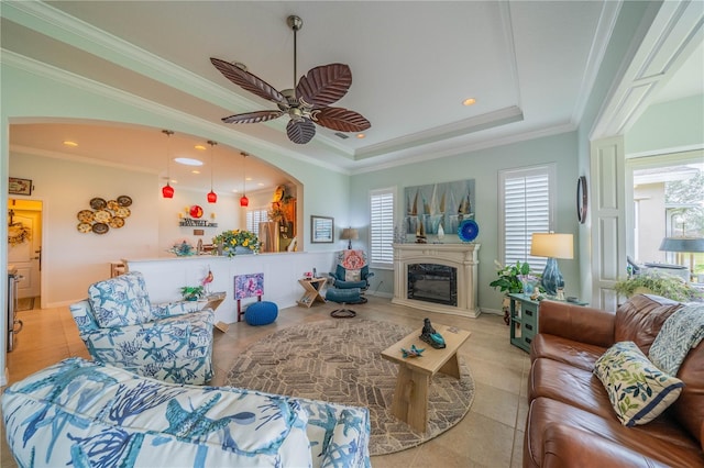 tiled living room featuring a raised ceiling, ornamental molding, and ceiling fan