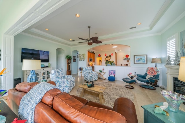 tiled living room with a fireplace, ornamental molding, a raised ceiling, and ceiling fan