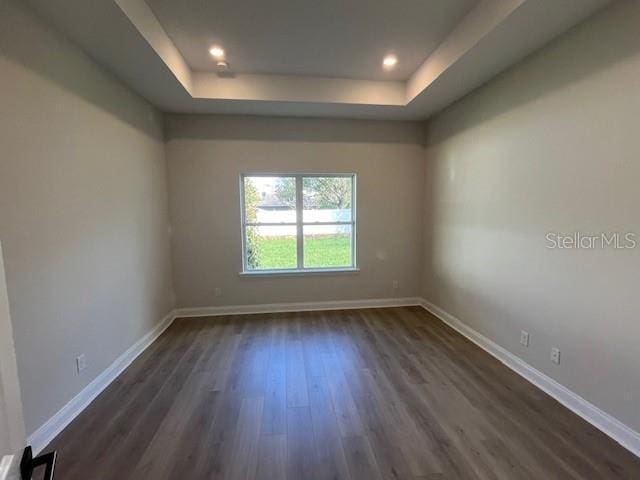 empty room featuring a tray ceiling, dark wood finished floors, baseboards, and recessed lighting