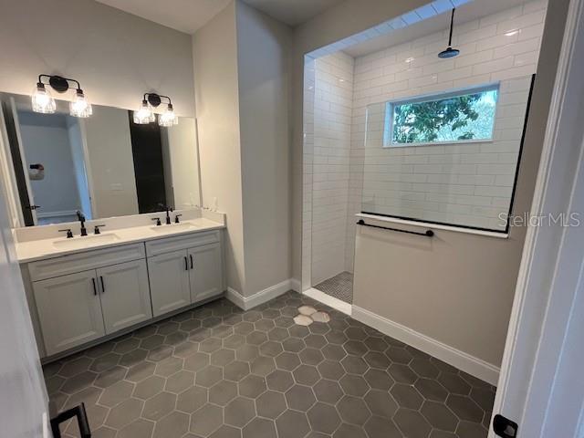 full bathroom featuring double vanity, baseboards, walk in shower, and a sink