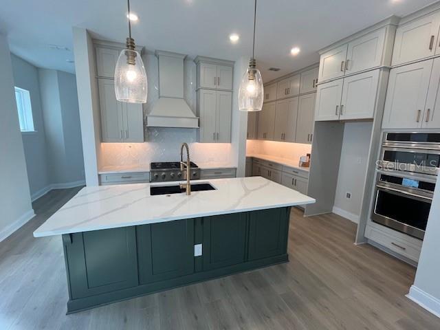 kitchen with custom range hood, light stone counters, a sink, and a center island with sink