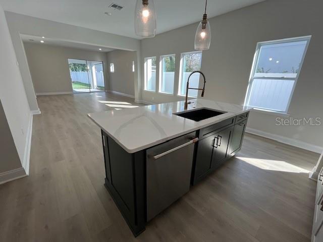 kitchen featuring a center island with sink, dishwasher, hanging light fixtures, dark cabinetry, and a sink