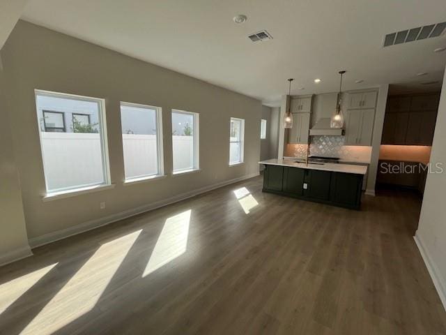 kitchen with visible vents, open floor plan, decorative light fixtures, light countertops, and wall chimney range hood