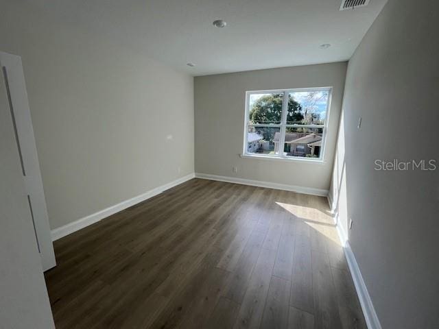 spare room with dark wood-style flooring, visible vents, and baseboards