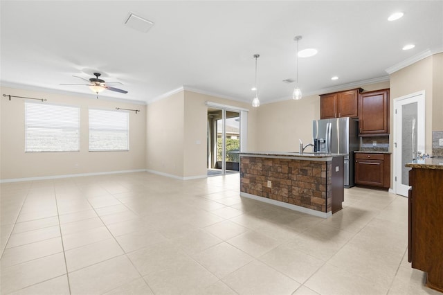 kitchen featuring crown molding, stainless steel fridge, ceiling fan, hanging light fixtures, and a center island with sink