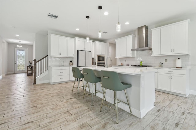 kitchen with pendant lighting, white cabinets, wall chimney exhaust hood, white refrigerator, and a center island with sink