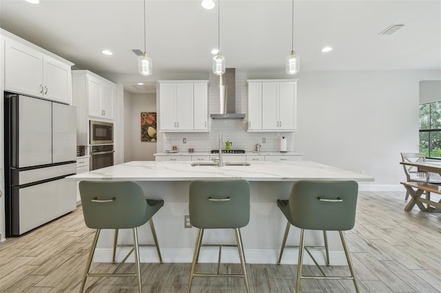 kitchen with black appliances, an island with sink, wall chimney range hood, and decorative light fixtures