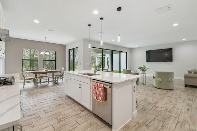 kitchen with hanging light fixtures, appliances with stainless steel finishes, sink, white cabinets, and an island with sink