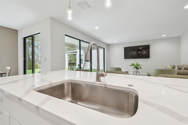 room details with decorative light fixtures, sink, white cabinetry, and light stone countertops