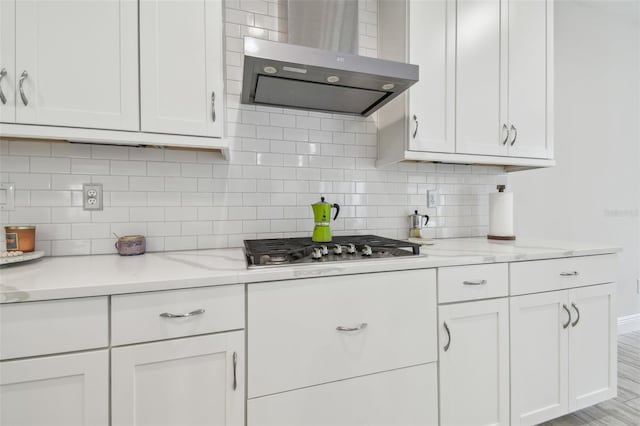 kitchen with light hardwood / wood-style flooring, wall chimney exhaust hood, white cabinetry, light stone counters, and stainless steel gas cooktop