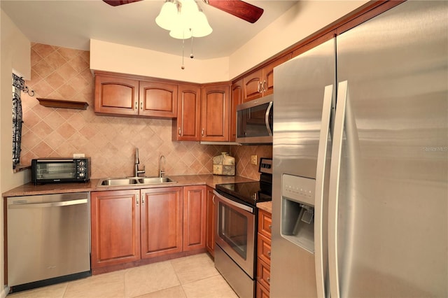 kitchen with light tile patterned flooring, appliances with stainless steel finishes, tasteful backsplash, sink, and ceiling fan