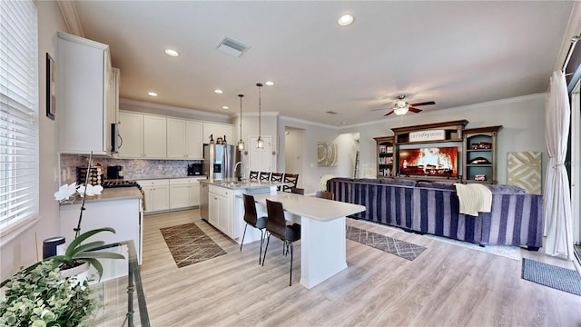 kitchen with white cabinetry, an island with sink, appliances with stainless steel finishes, decorative backsplash, and decorative light fixtures