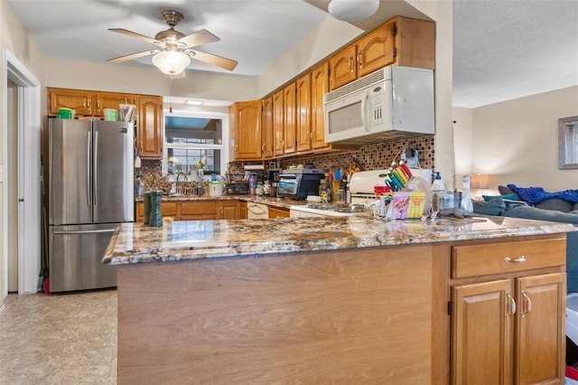 kitchen featuring kitchen peninsula, ceiling fan, backsplash, stainless steel refrigerator, and light stone counters