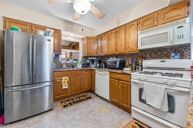 kitchen with white appliances, sink, backsplash, ceiling fan, and light stone counters