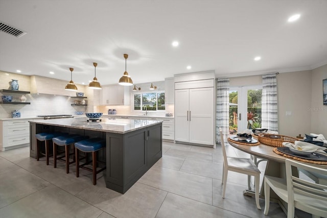 kitchen featuring paneled built in refrigerator, decorative light fixtures, white cabinets, and a center island