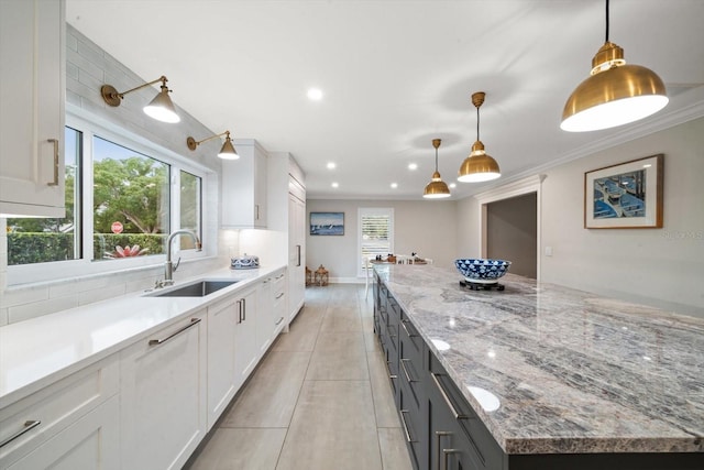 kitchen featuring light stone countertops, white cabinets, hanging light fixtures, and sink