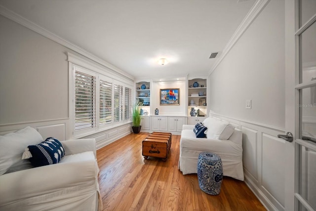 living room with built in shelves, light hardwood / wood-style flooring, and ornamental molding