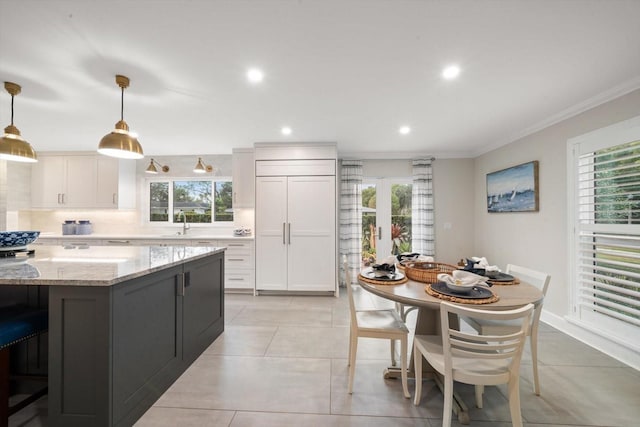 kitchen with pendant lighting, light stone countertops, white cabinetry, and paneled fridge