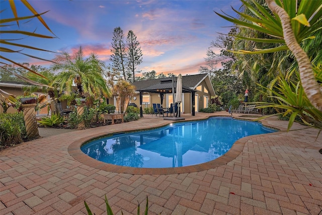 pool at dusk with a gazebo and a patio area