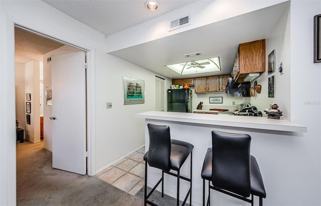 204 Lennox Rd W, W, Palm Harbor, FL 34683 - kitchen with light colored carpet, a kitchen breakfast bar, kitchen peninsula, and black fridge