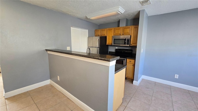 kitchen with light tile patterned floors, kitchen peninsula, appliances with stainless steel finishes, and a textured ceiling