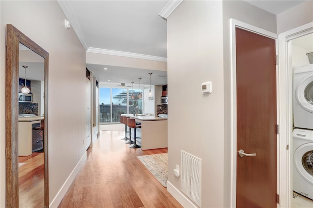 laundry room with stacked washer / drying machine, light wood-type flooring, and crown molding