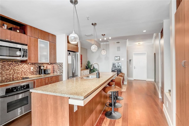 kitchen with decorative light fixtures, sink, a kitchen island with sink, appliances with stainless steel finishes, and a kitchen breakfast bar