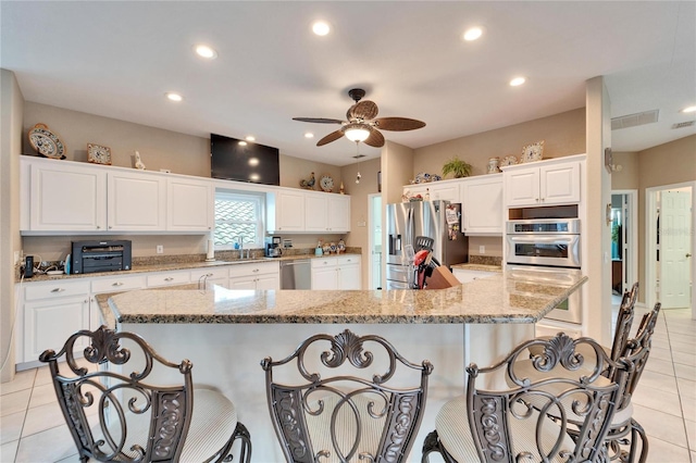 kitchen with a kitchen breakfast bar, a spacious island, white cabinets, light stone countertops, and stainless steel appliances