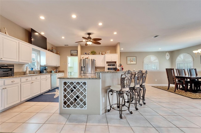 kitchen with appliances with stainless steel finishes, white cabinets, light tile patterned floors, stone counters, and a kitchen island