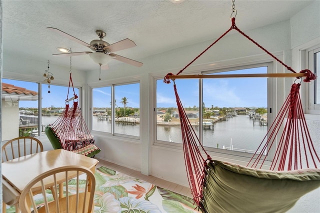 sunroom with ceiling fan and a water view