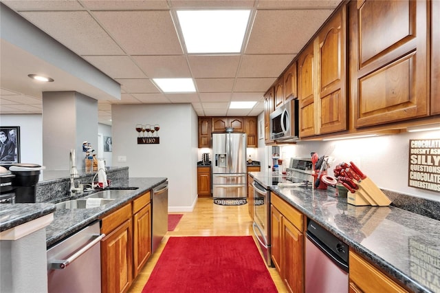 kitchen featuring dark stone countertops, a drop ceiling, appliances with stainless steel finishes, and light wood-type flooring